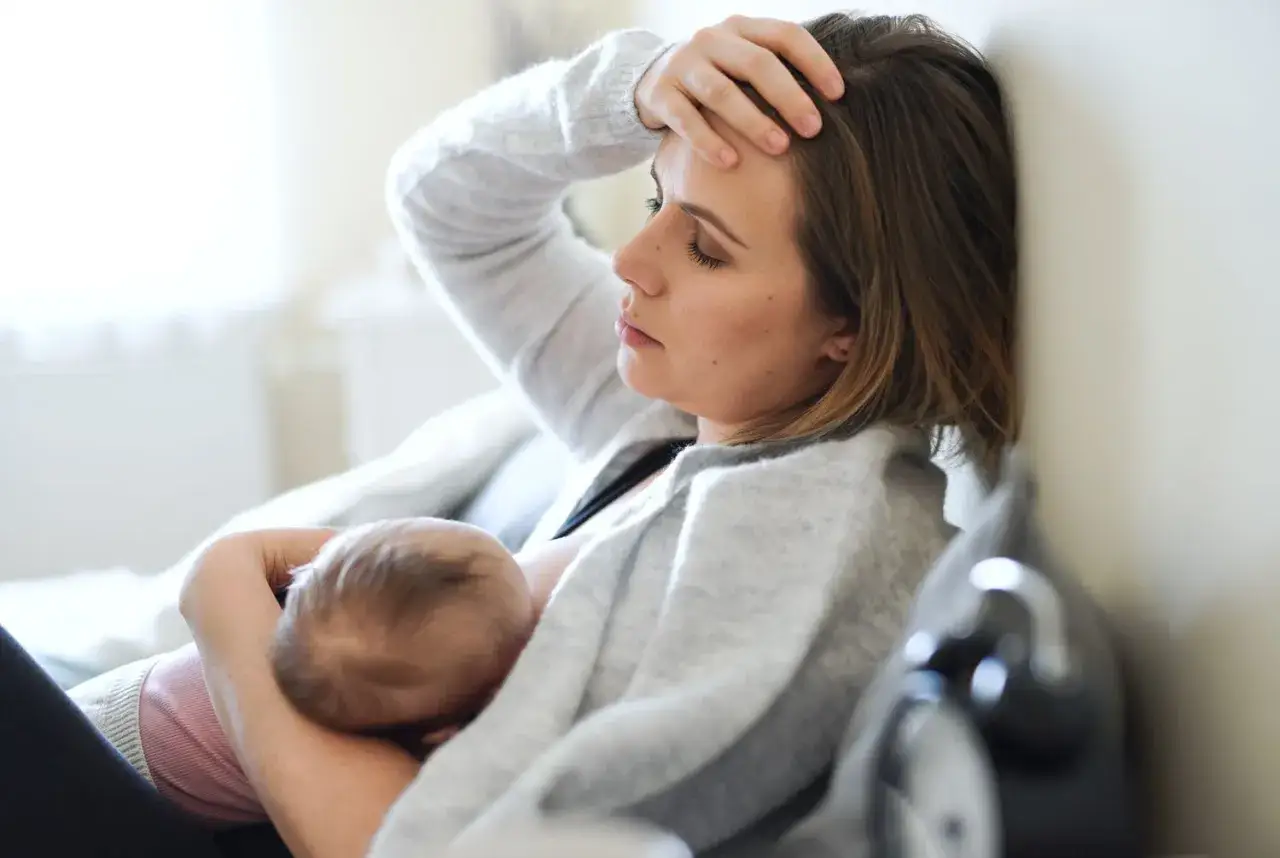 M&uuml;de Mutter stillt Baby, Hand an der Stirn. M&ouml;gliche baby koffein symptome wie Unruhe k&ouml;nnten die Ursache sein.