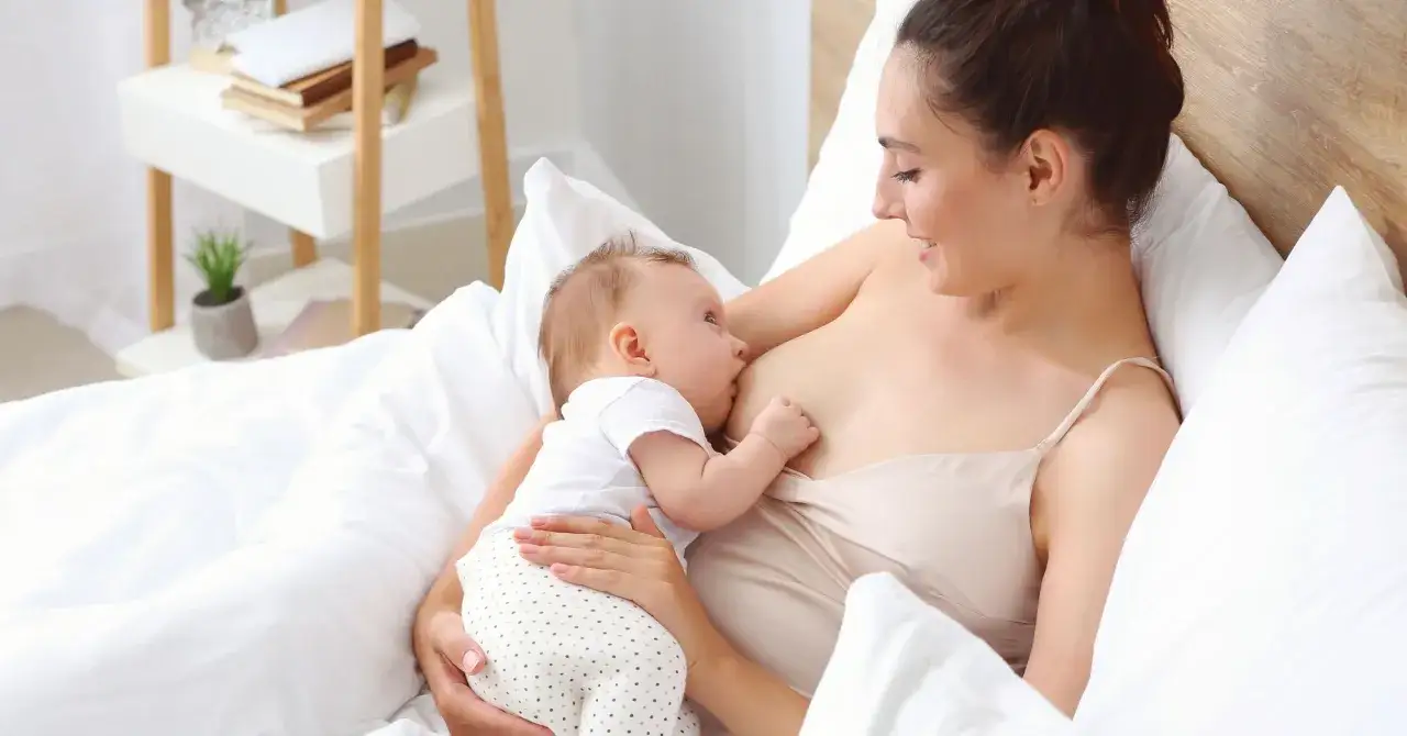 Eine Mutter stillt ihr Baby im Bett. Ein Moment der Ruhe und Verbundenheit, eine stille Empfehlung für die natürliche Ernährung.