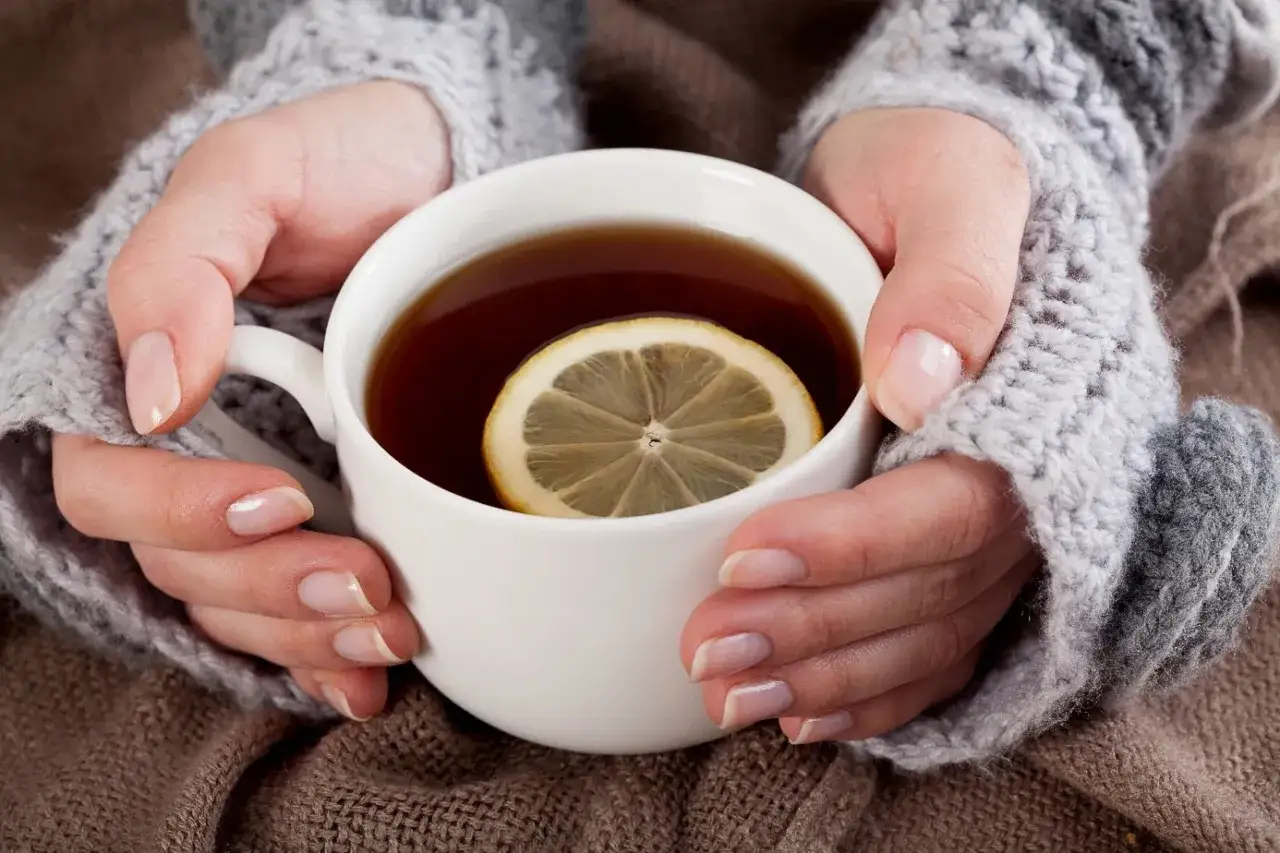Hände in Strickstulpen halten eine Tasse Tee mit Zitronenscheibe. Perfekt für eine gemütliche Tee Stillzeit.