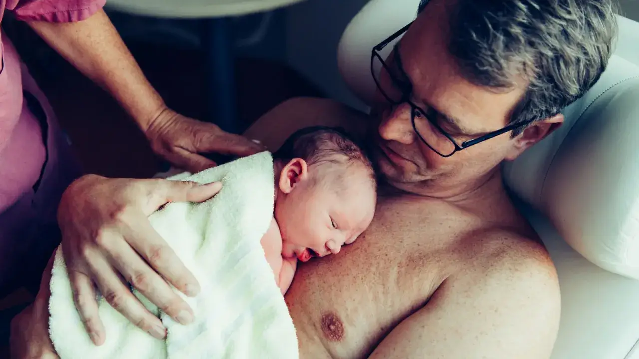 Vater h&auml;lt Neugeborenes auf der Brust. Die N&auml;he zeigt die Vorteile stillen, eine tiefe Bindung.
