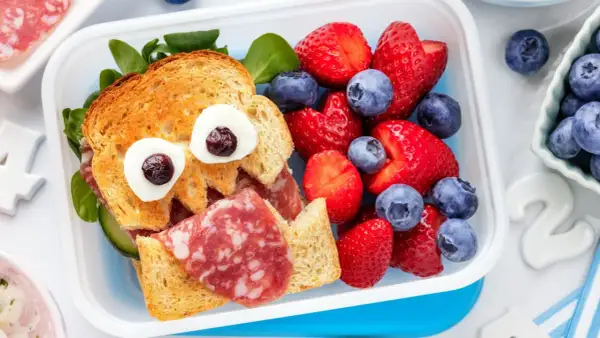 Ein lustiges Vesper-Essen Kita: ein Toast-Gesicht mit Wurst, Gurke und Beeren.