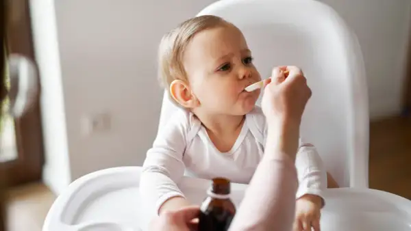 Ein Baby im Hochstuhl erhält Medikamente per Löffel. Die Eltern wechseln zwischen Ibuprofen und Paracetamol alle 4 Stunden, um Fieber zu senken.