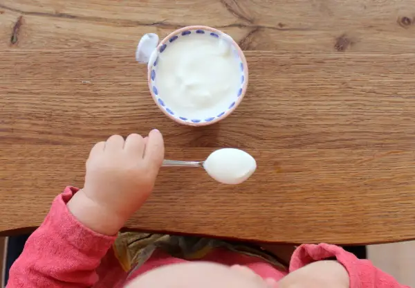 Kleiner Löffel mit Joghurt für ein Baby. Wann ist Joghurt für Babys geeignet?