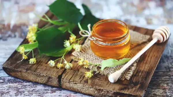 Ein Glas Honig mit Lindenblüten und einem Honiglöffel. Perfekt zum Honig essen beim Stillen für süße Momente.