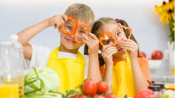 Zwei Kinder mit Paprikaringen vor den Augen, die Spaß beim Kochen haben. Ein wichtiger Aspekt für gesunde Entwicklung ist der richtige kalorienbedarf kind 10 jahre.