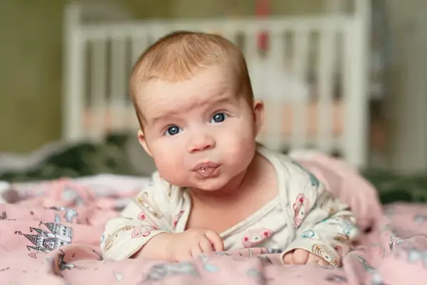 Baby mit blauen Augen liegt auf dem Bauch, sabbert und übt den 4 monats schub.