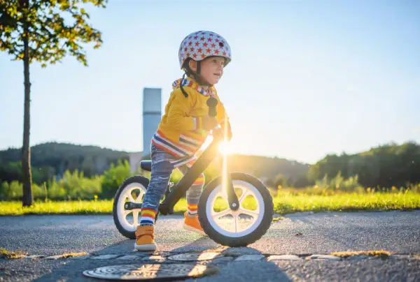 Kleiner Junge mit Helm auf Laufrad, strahlend im Sonnenuntergang. Ein echter Entwicklungsschub mit 3 Jahren!