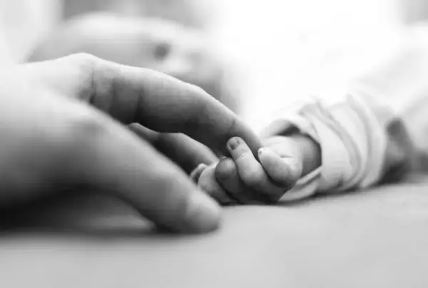 Ein Erwachsenenfinger berührt die winzige Hand eines Babys, das den Greifreflex zeigt.