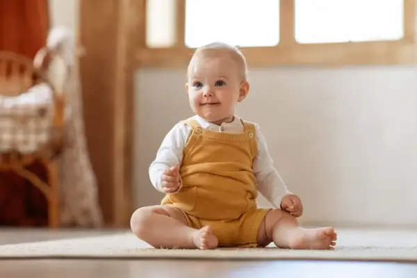 Ein fröhliches Baby sitzt auf dem Teppich. Die meisten Babys können ab dem 6. Monat sitzen.