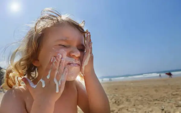 Kind schmiert sich Sonnencreme ins Gesicht. Bei Sonnenbrand helfen Hausmittel wie Quark oder Aloe Vera.
