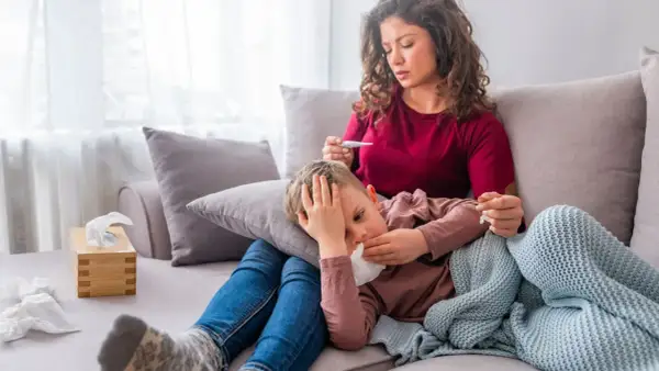 Besorgte Mutter misst Fieber bei ihrem Kind, das unter Untertemperatur leidet und schwitzt. Ein Taschentuch liegt bereit.