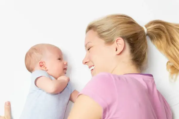 Ein lächelndes Baby, 2 Wochen alt, schaut seine Mutter an. Sie liegt neben ihm und lächelt zurück.