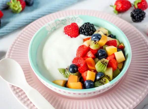 Ein Schüsselchen Joghurt mit frischem Obstsalat, perfekt für ein Kleinkind. Erdbeeren, Blaubeeren, Kiwi und Pfirsichstücke machen den Joghurt zum Genuss.