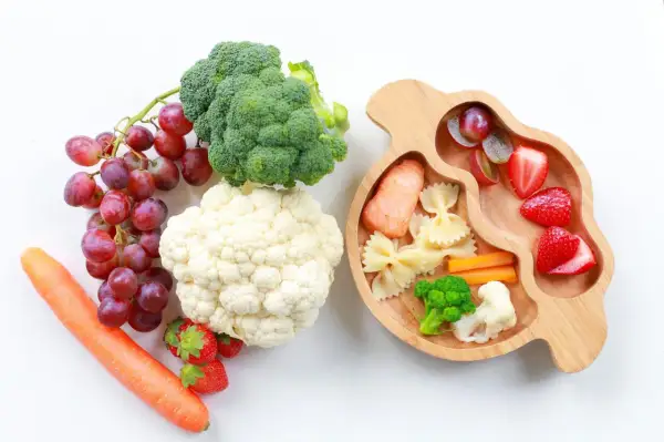 Baby led weaning rezepte: Lachs, Nudeln, Gemüse und Obst auf einem Holztablett.