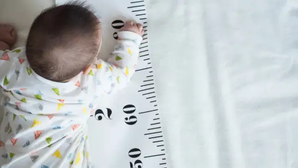 Baby liegt auf einer Messlatte, die als **Kleinwuchs Tabelle** dient. Die Messlatte zeigt Zentimeterangaben.