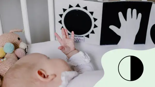Ein Baby mit 2 Wochen erkundet mit seiner Hand ein Schwarz-Weiß-Buch mit Sonne und Hand.